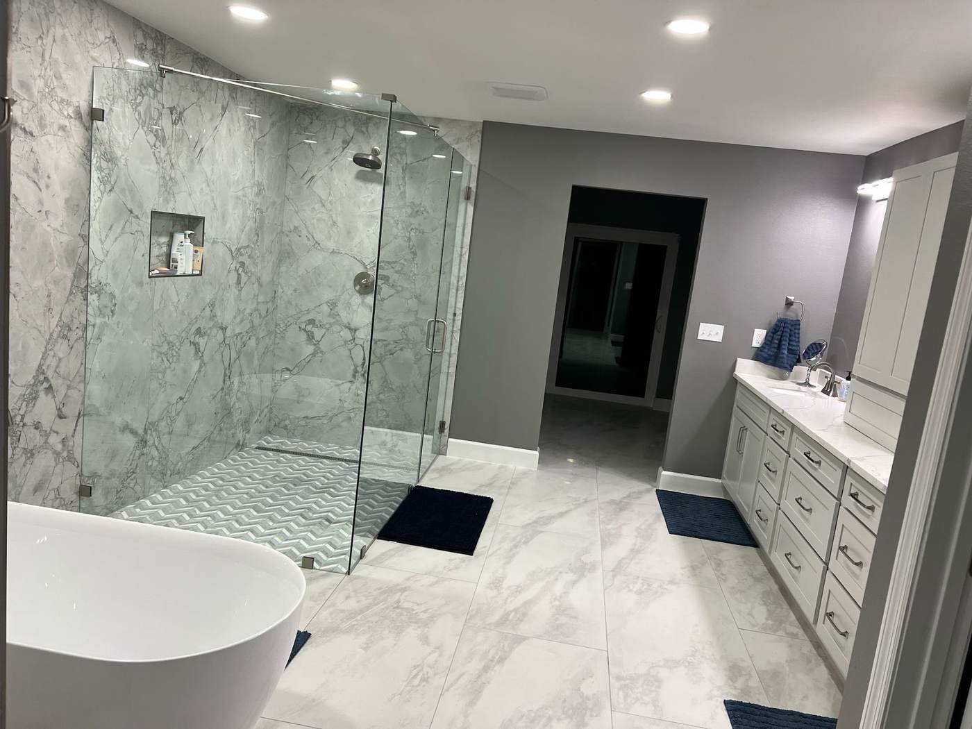 Remodeled bathroom with a glass-enclosed marble-look tile shower, freestanding tub and tile floor