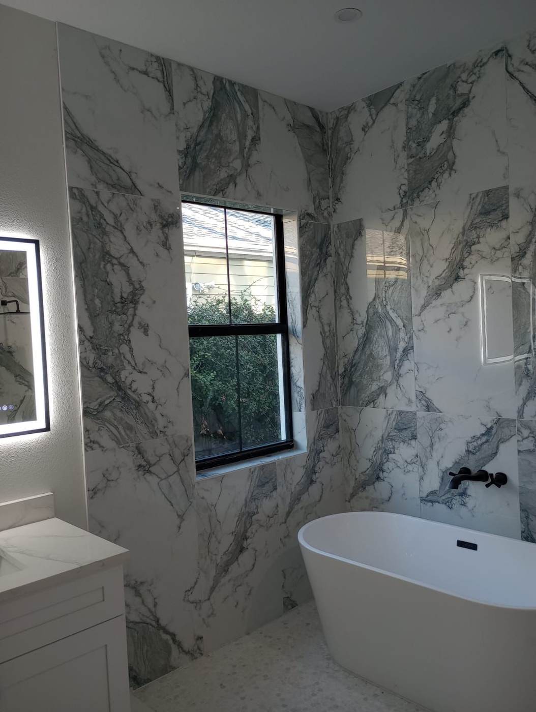Marble-look wall tile beside a freestanding tub and a window.