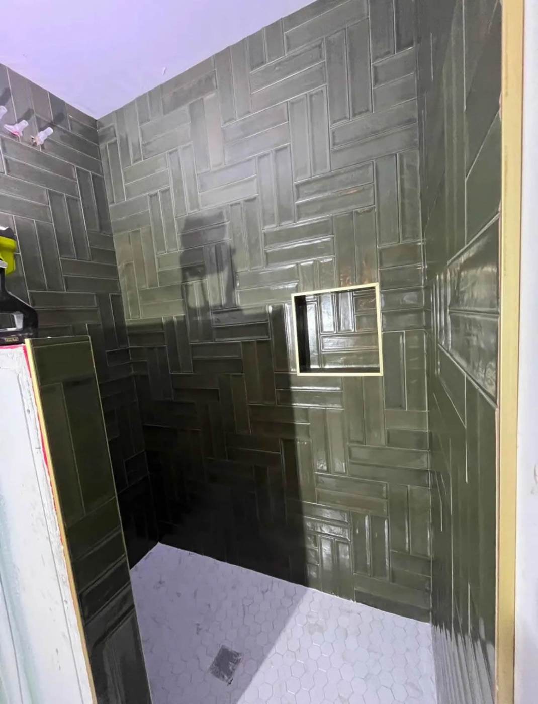 Dark green herringbone tile on a walk-in shower wall with a recessed niche